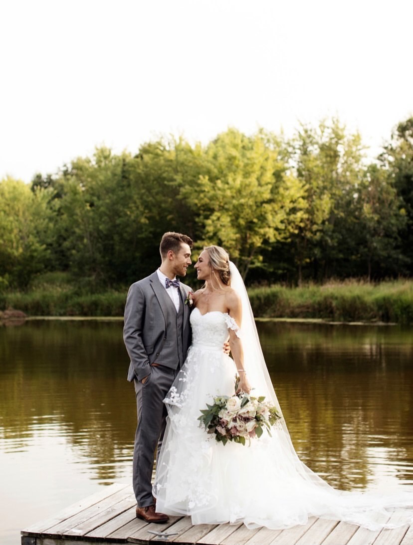 A bride in her customized Casablanca wedding dress and groom in his grey suit by a lake on their wedding day. 